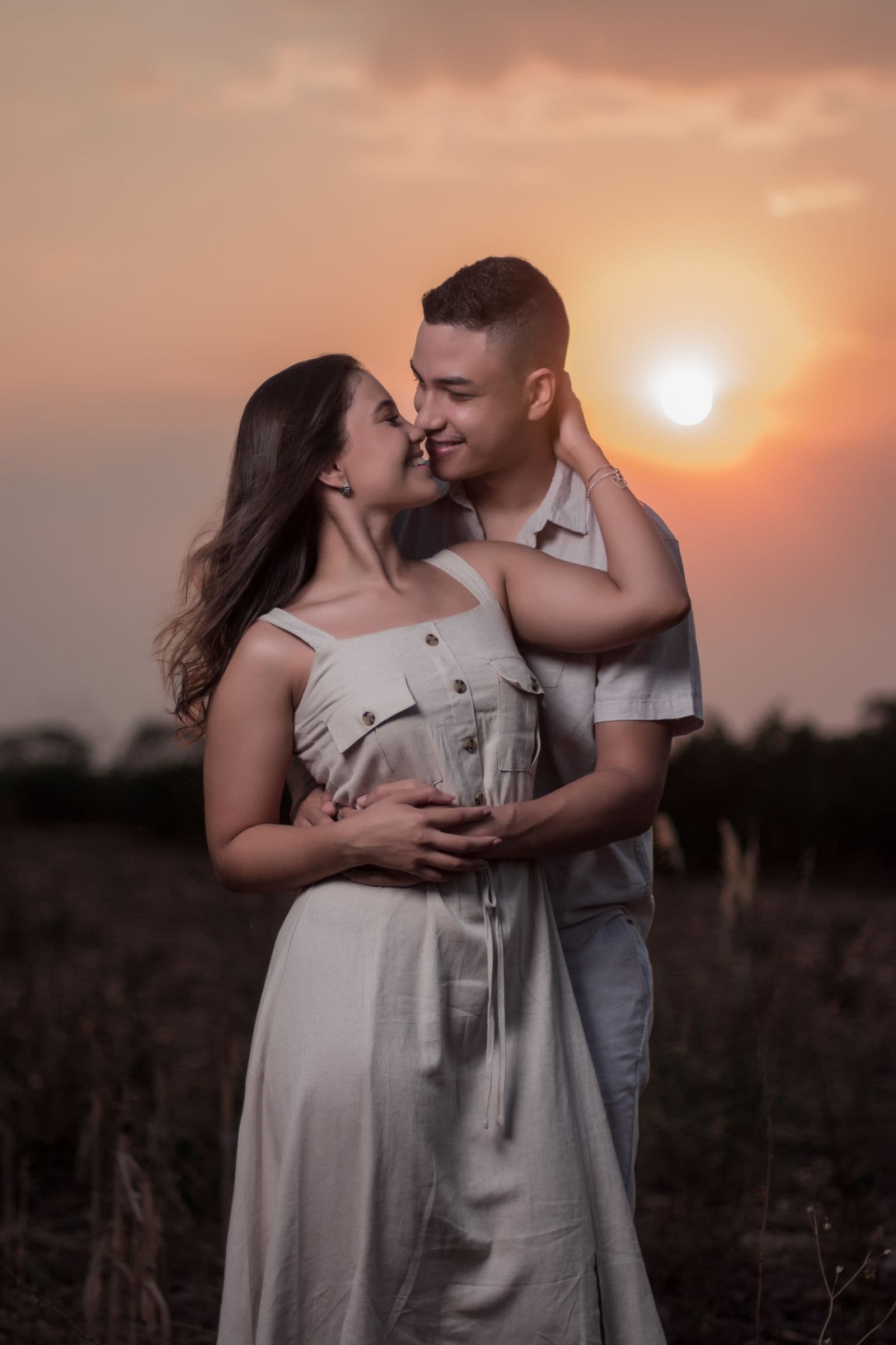 Casal se abraçando em um campo ao pôr do sol
